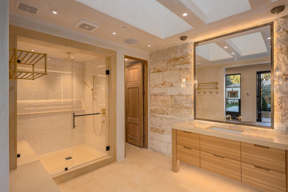 Bathroom with glass-enclosed shower room, wide mirror, marble sink and wooden cabinetry.