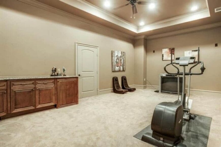 The media room is filled with built-in cabinets, a TV, and gym equipment.