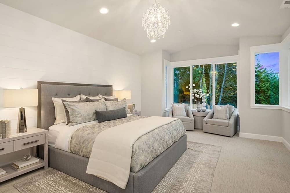 Primary bedroom with a vaulted ceiling, carpeted floor, and a sitting area by the boxed bay window.