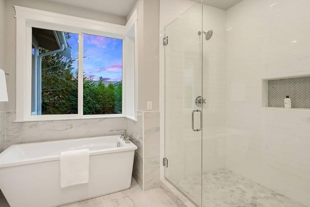 Primary bathroom with a walk-in shower and a freestanding tub situated under the sliding windows.