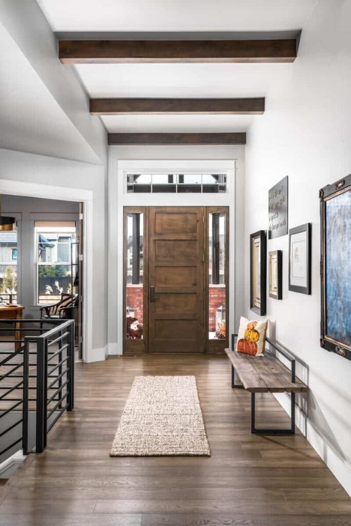 Foyer with a beamed ceiling, a wooden bench, and light gray walls adorned with framed artworks.