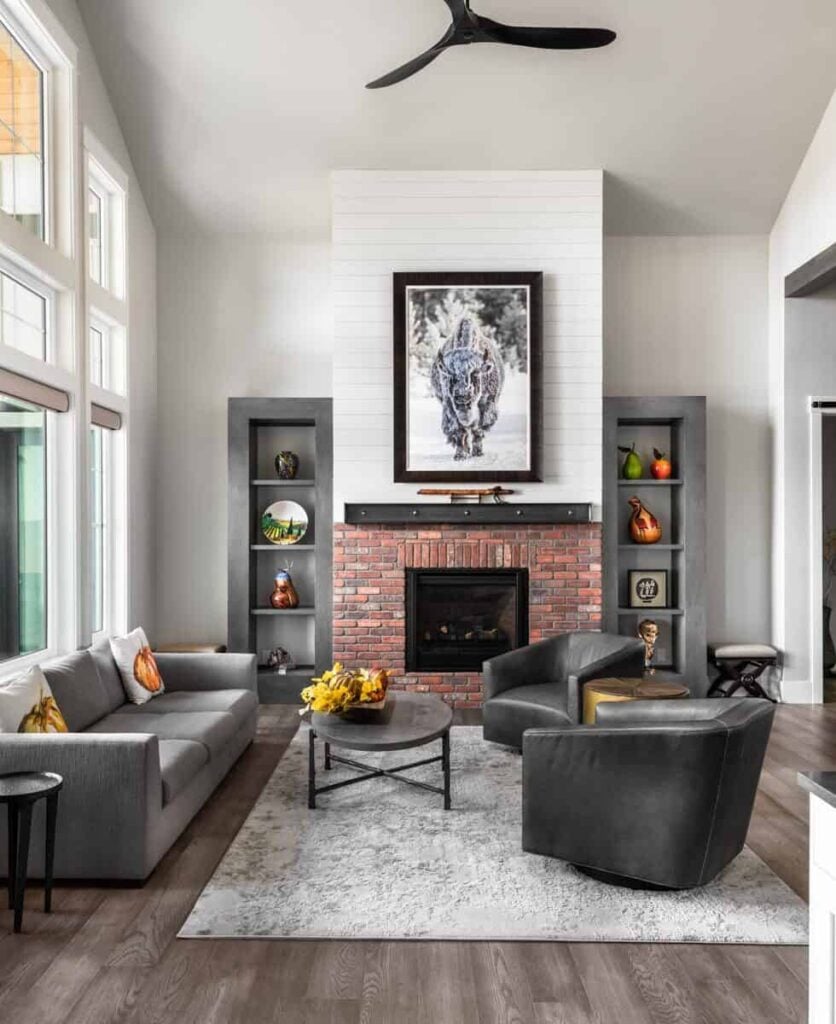 Family room with a gray sectional, leather armchairs, and a brick fireplace flanked by built-in shelves.