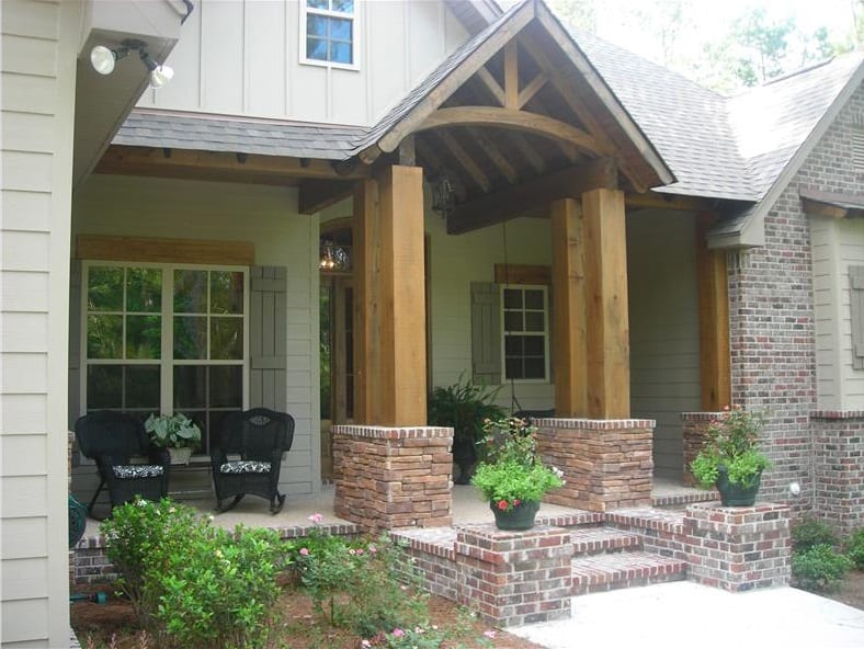 A closer look at the covered front porch with stone columns, wooden trims, and wicker rocking chairs.