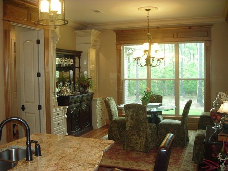 Dining area with white and dark wood cabinets, skirted chairs, and a round glass-top table illuminated with a warm chandelier.