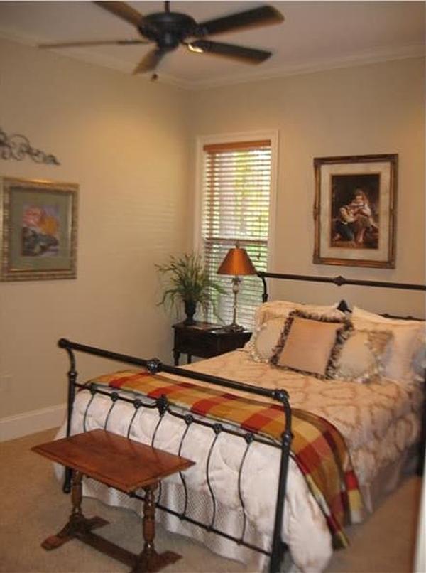 The primary bedroom has carpet flooring and a wrought iron bed complemented with a wooden table at its end.