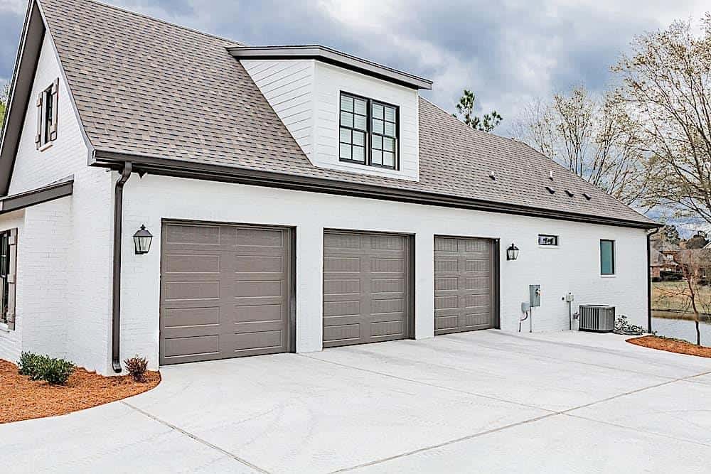 Side exterior view with a large shed dormer and a 3-car garage enclosed in dark-paneled doors.