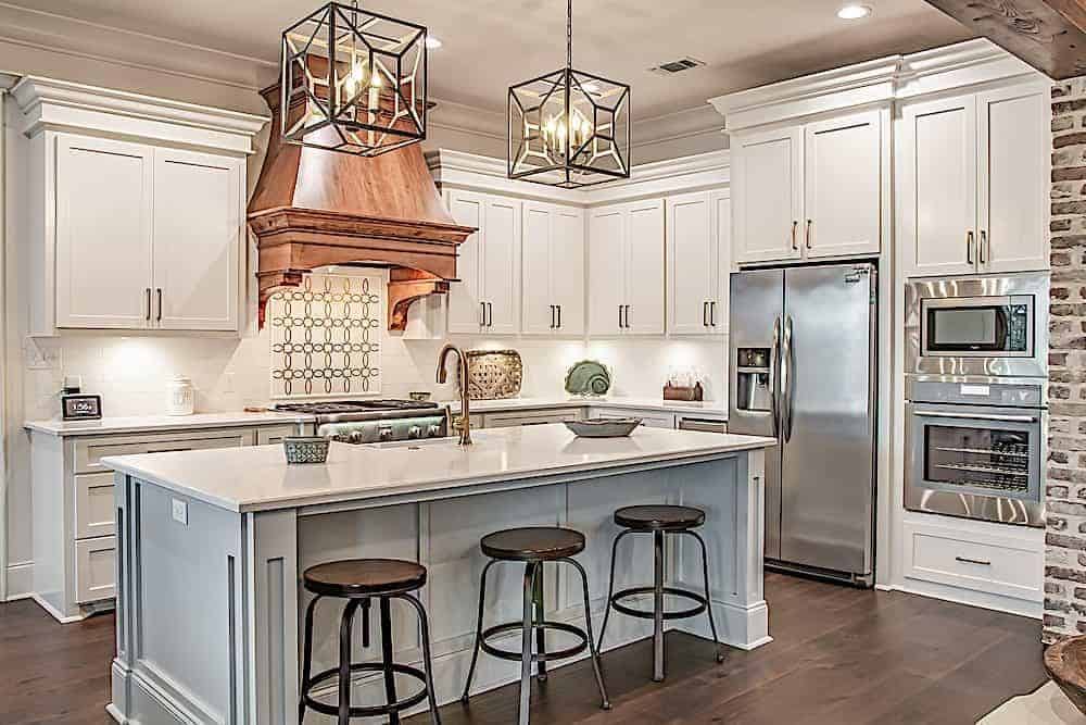 The kitchen is equipped with stainless steel appliances, white cabinetry, and a breakfast island paired with round bar stools.