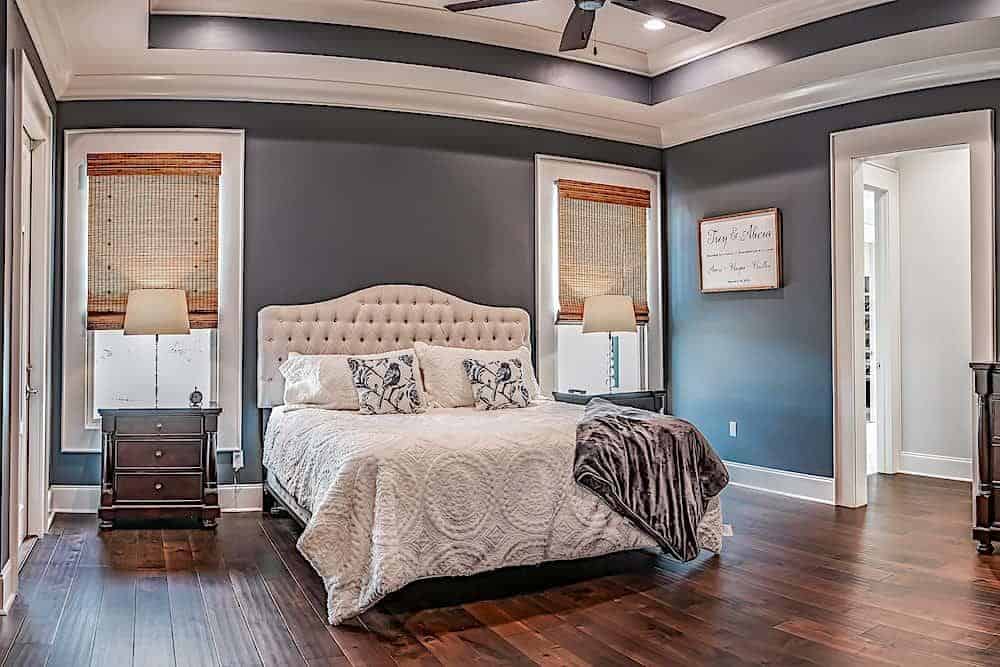 The primary bedroom has a hardwood floor, gray walls, and a tray ceiling mounted with a fan.