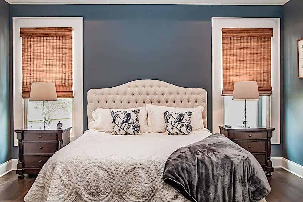 Matching nightstands and narrow windows flank the white tufted bed.