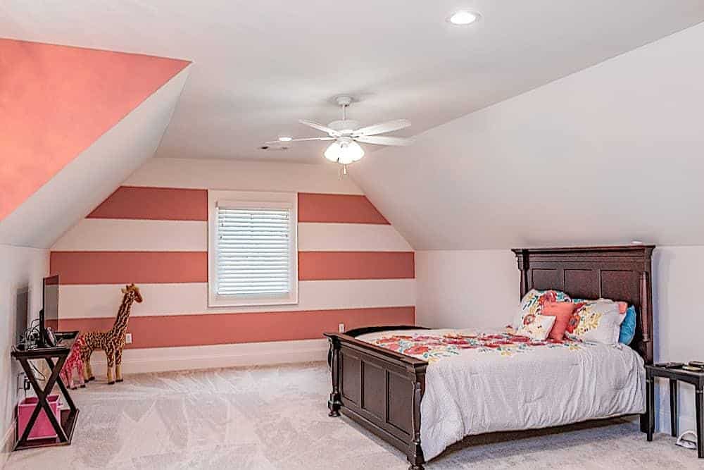 This bedroom has a vaulted ceiling and white walls accentuated with salmon pink stripes.