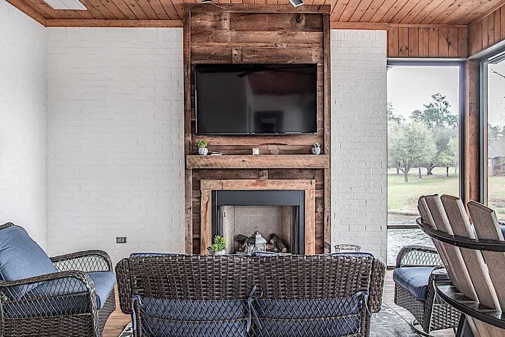 Covered porch with wicker cushioned seats and a fireplace topped with a wall-mounted TV.