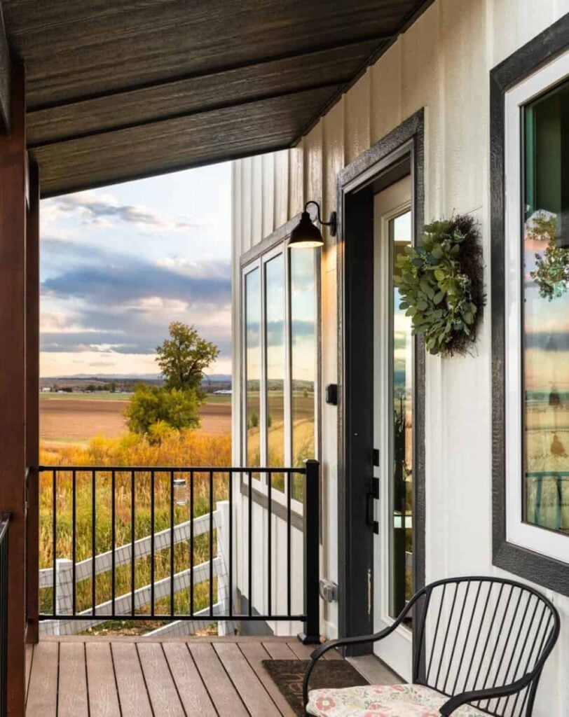 The covered deck has a glazed entry door and a round-back chair over wood plank flooring.
