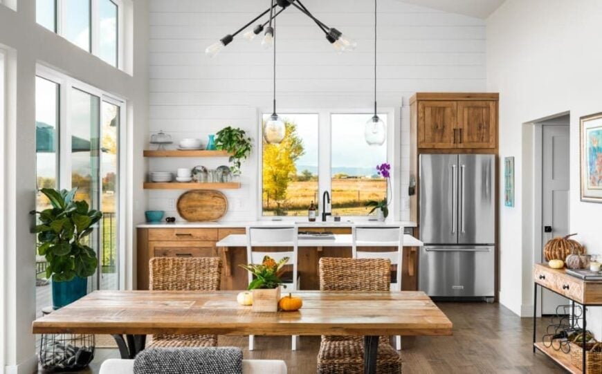 The kitchen on the other end offers stainless steel appliances, a cooktop island, wooden cabinets, and floating shelves fixed against the white shiplap wall.
