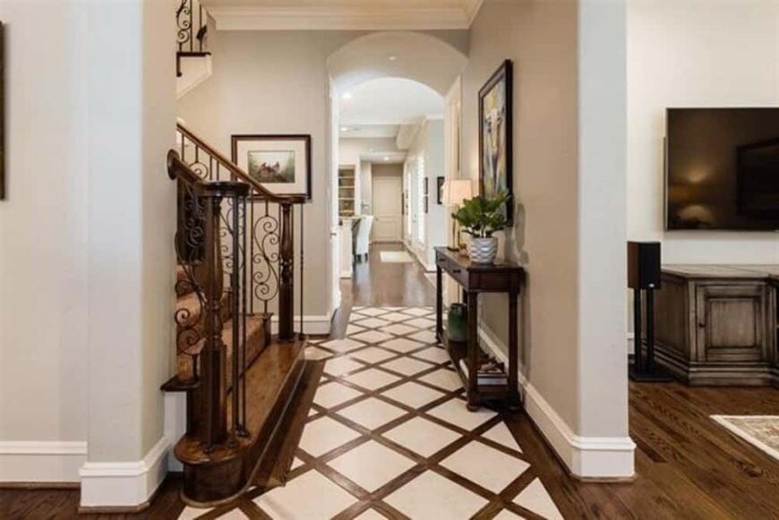 Foyer with a custom floor, an intricate staircase, and a dark wood console table topped with framed artwork.