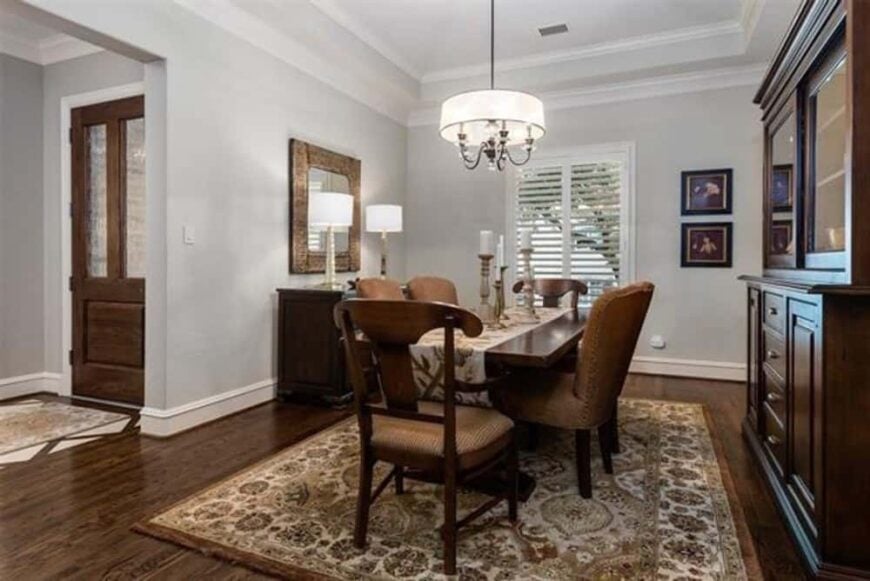 The formal dining room offers wooden cabinets, a 6-seater dining set, and a drum chandelier that hangs from the tray ceiling.