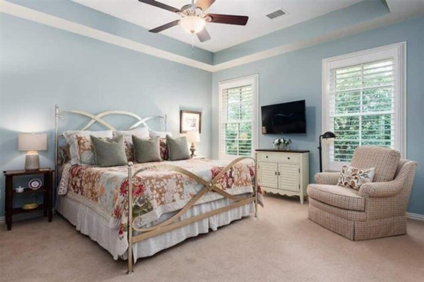 This bedroom has carpet flooring, light blue walls, and a couple of windows bringing natural light in.