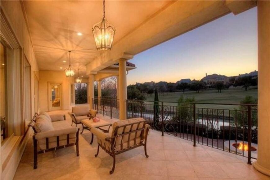 The veranda has cushioned seats, ambient lighting, and wrought iron railings overlooking the expansive greenery.