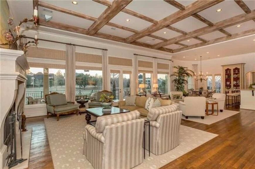 Family room with a beamed ceiling, a fireplace, fabric upholstered seats, and a rear wall of windows overlooking the rear veranda.