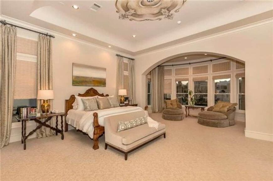 The primary bedroom has a carpeted floor, a tray ceiling, and a spacious sitting area by the bow window.