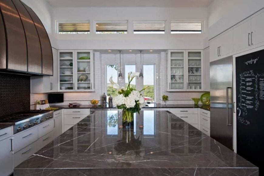 The kitchen is equipped with stainless steel appliances, granite countertops, white cabinetry, and an immense center island.
