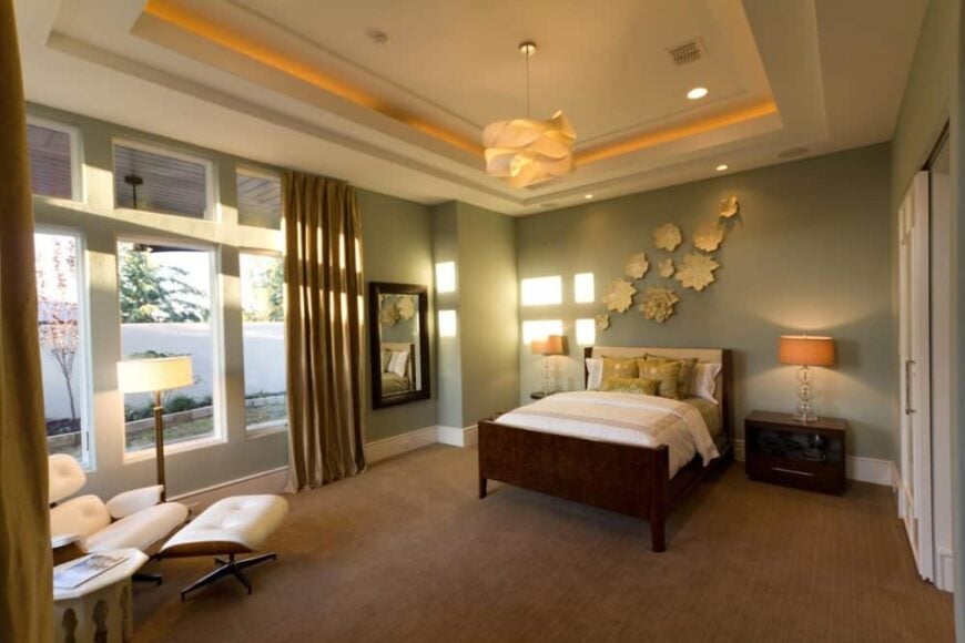 Primary bedroom with a tray ceiling, carpeted floor, and plenty of windows bringing ample natural light in.