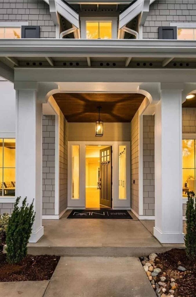 Covered entry with large columns and a wooden front door illuminated with a warm pendant light.
