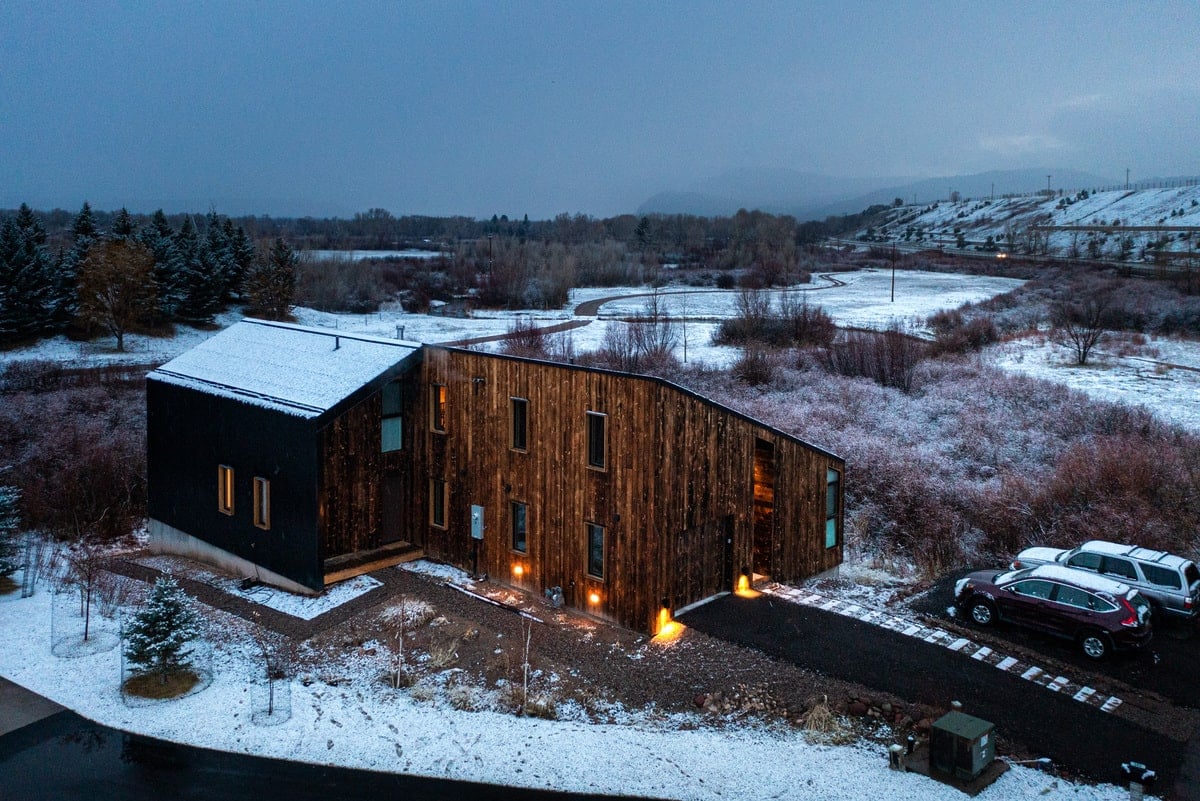An aerial view of the house during winter with two cars in an open garage.