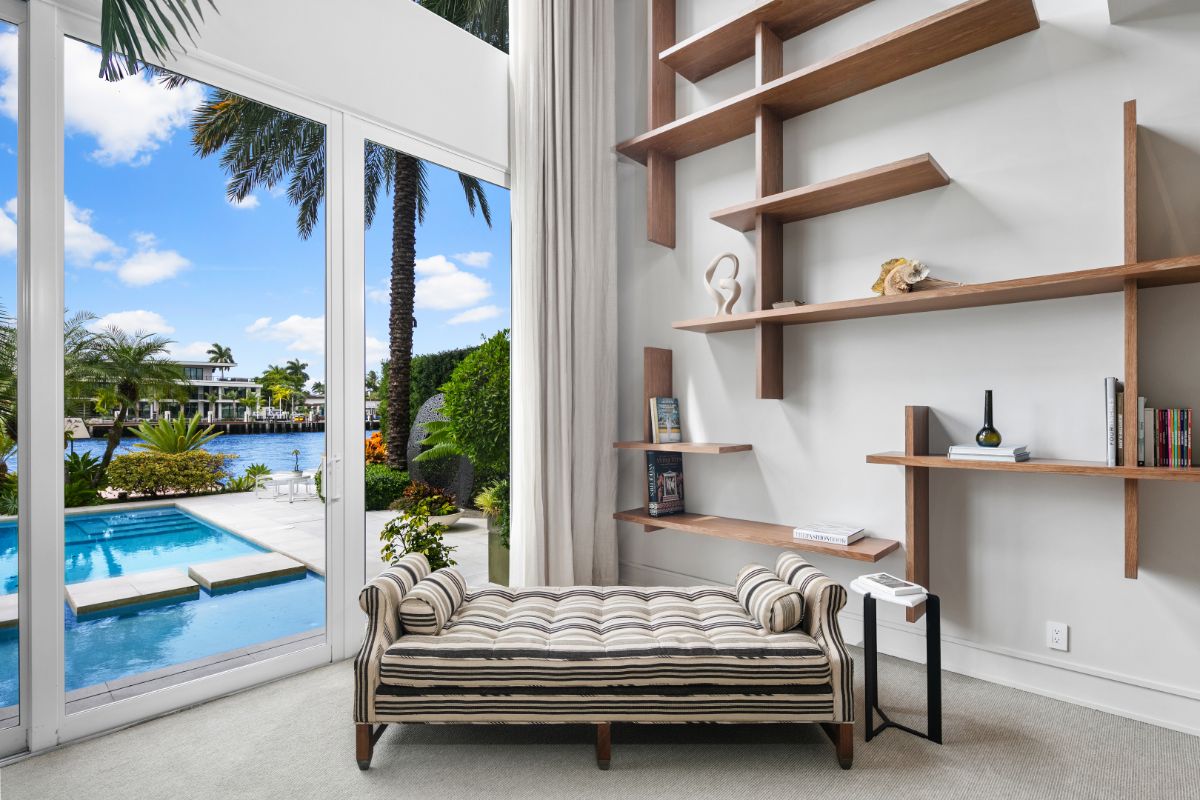 Modern design master bedroom with full height glass wall facing the river and sofas beneath the wall shelves.