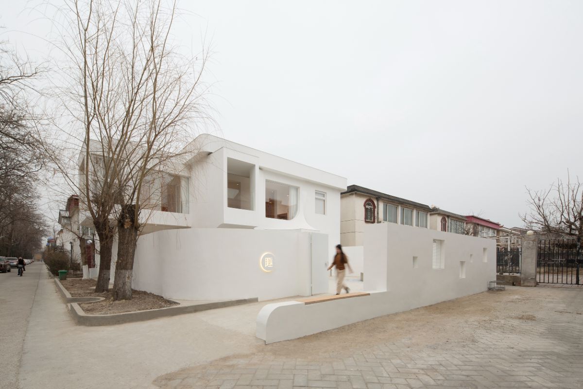 A full-length exterior shot of the house on the corner of the street, with a woman walking along the pathway.