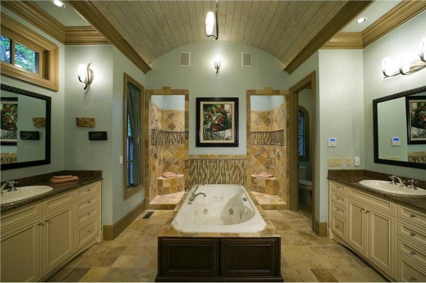 Primary bathroom with a spacious walk-in shower, separate his and her sink vanities, and a central bathtub crowned with a barrel-vaulted ceiling.