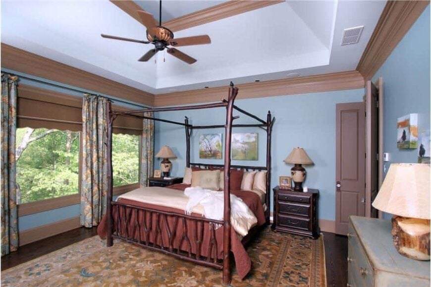 The primary bedroom features a coved ceiling, a four-poster bed, and light blue walls lined with brown moldings.