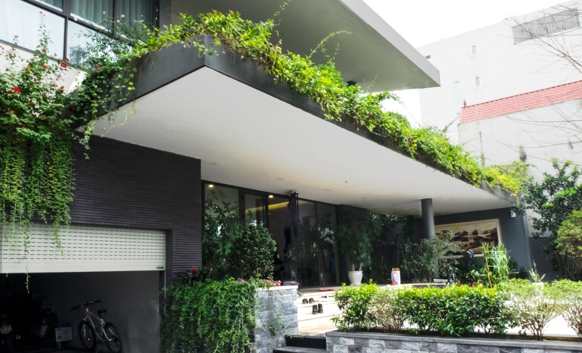 The main entrance of the house, with a large glass wall system and vegetation covering and protecting the large balcony.
