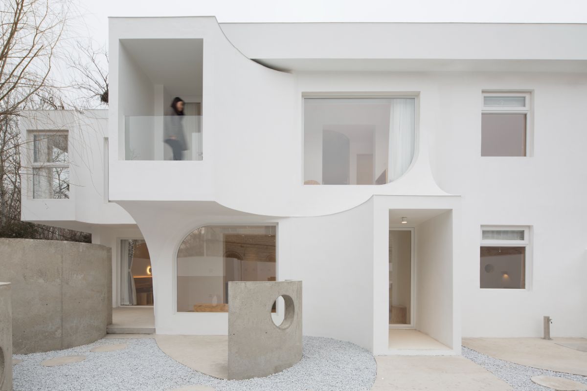 The house's white facade is based on a quarter-arc design, with a woman on the second floor terrace.