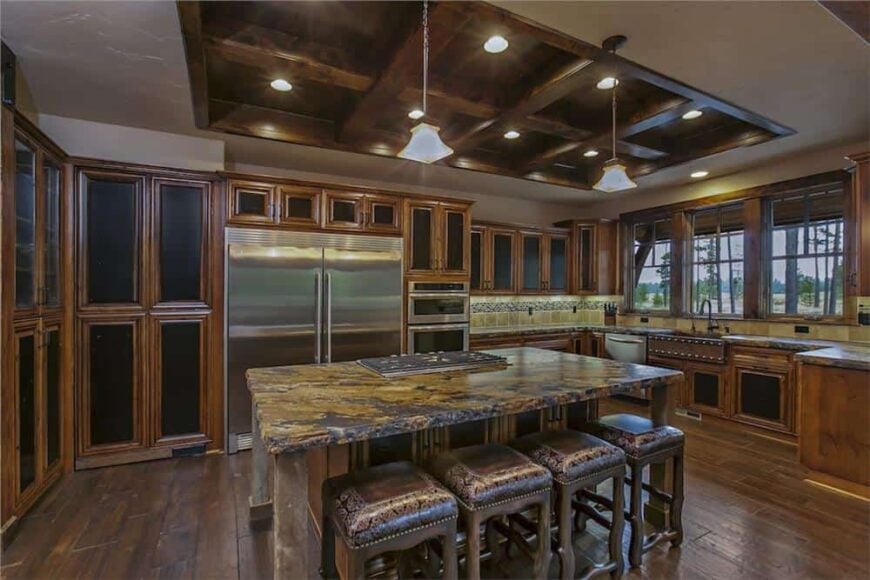Kitchen with stainless steel appliances, wooden cabinetry, and a breakfast island crowned with a coffered ceiling.