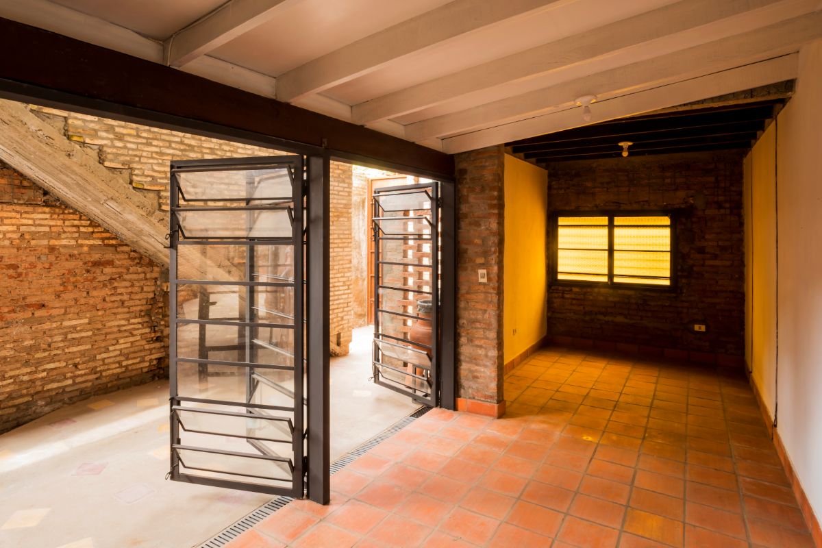 An open first-floor interior space with a shed-beamed ceiling and a brick wall.