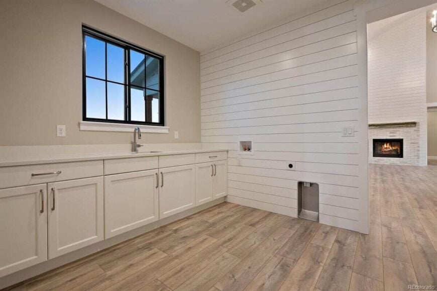 The mudroom has white cabinets and a utility sink topped with a framed window.
