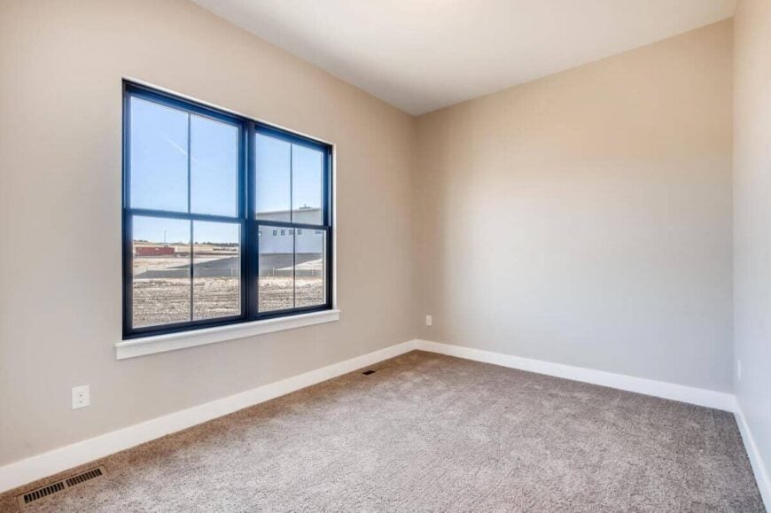 This bedroom has a carpeted floor and light gray walls lined with white base moldings.