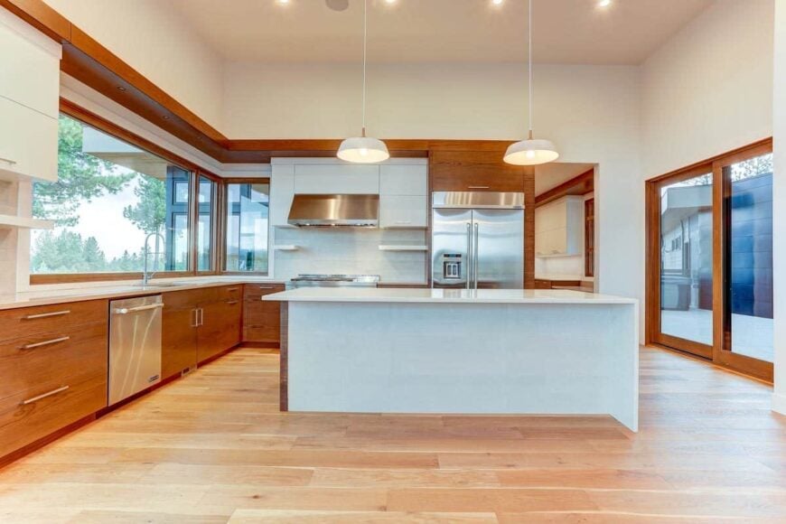 The kitchen features white and wooden cabinets, stainless steel appliances, and a breakfast island topped with a couple of dome pendants.