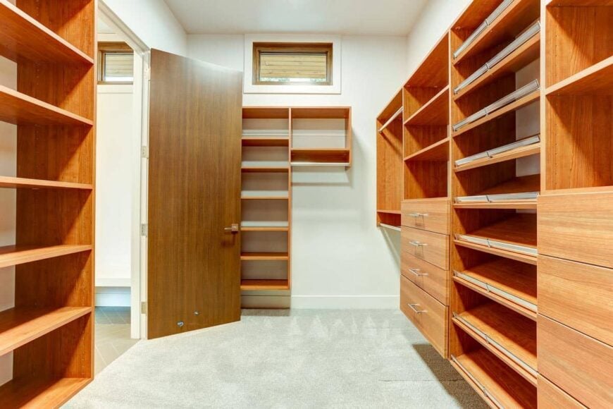 The primary walk-in closet is filled with rich wooden shelves contrasting the white walls.