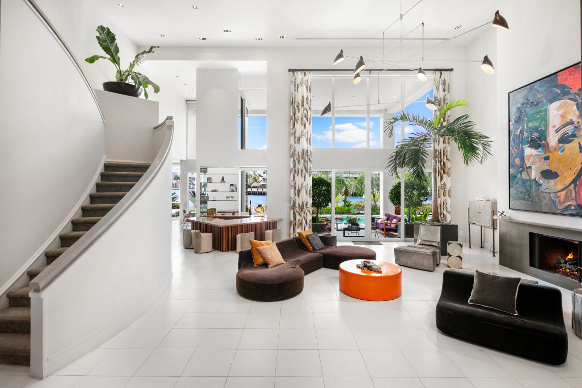 Two story living area with full lenght glass wall, cushioned sofas, and concrete fireplace.