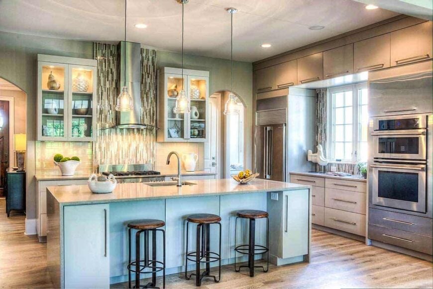 The kitchen offers stainless steel appliances, light gray cabinetry, and a breakfast island well-lit by glass dome pendants.