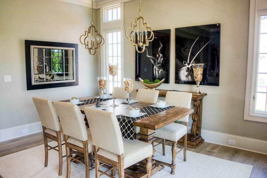 Dining room with a rectangular dining set, stylish brass pendants, and beige walls adorned with deer artworks and a decorative mirror.