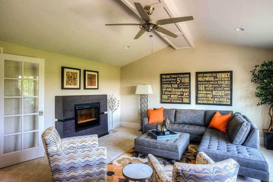 A fireplace and L-shaped sofa accentuated with orange pillows complete the media room.