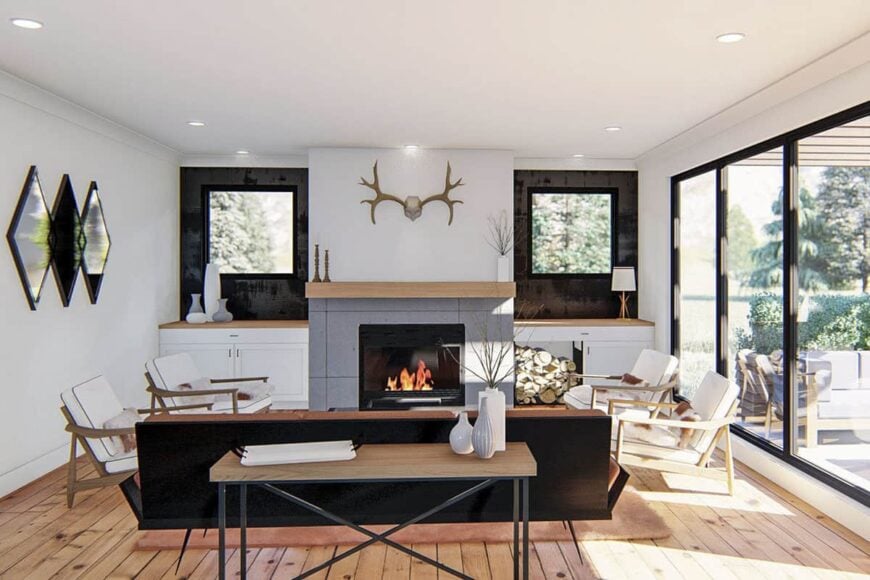 The great room offers white cushioned chairs and a glass-enclosed fireplace flanked by base cabinets and picture windows.