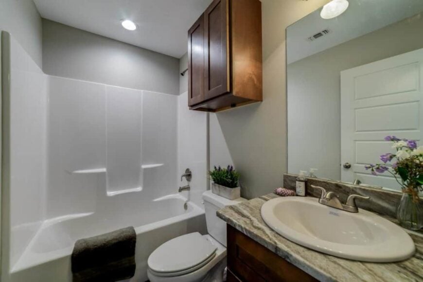 This bathroom is equipped with a sink vanity, a tub and shower combo, and a toilet topped with an overhead cabinet.