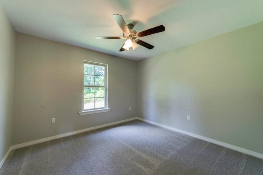 Another bedroom with carpeted floor, a ceiling fan, and gray walls lined with white moldings.