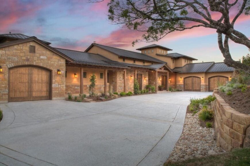 Front exterior view showcasing its stone and stucco siding, metal roofs, multiple garages, and a deep covered porch framed with wooden columns.