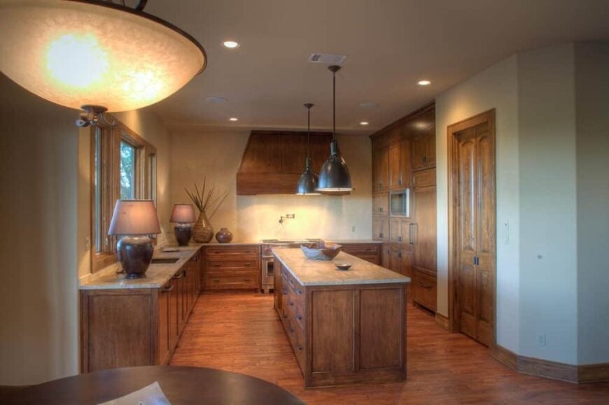 The kitchen offers natural wood cabinetry, granite countertops, and a center island topped with black dome pendants.