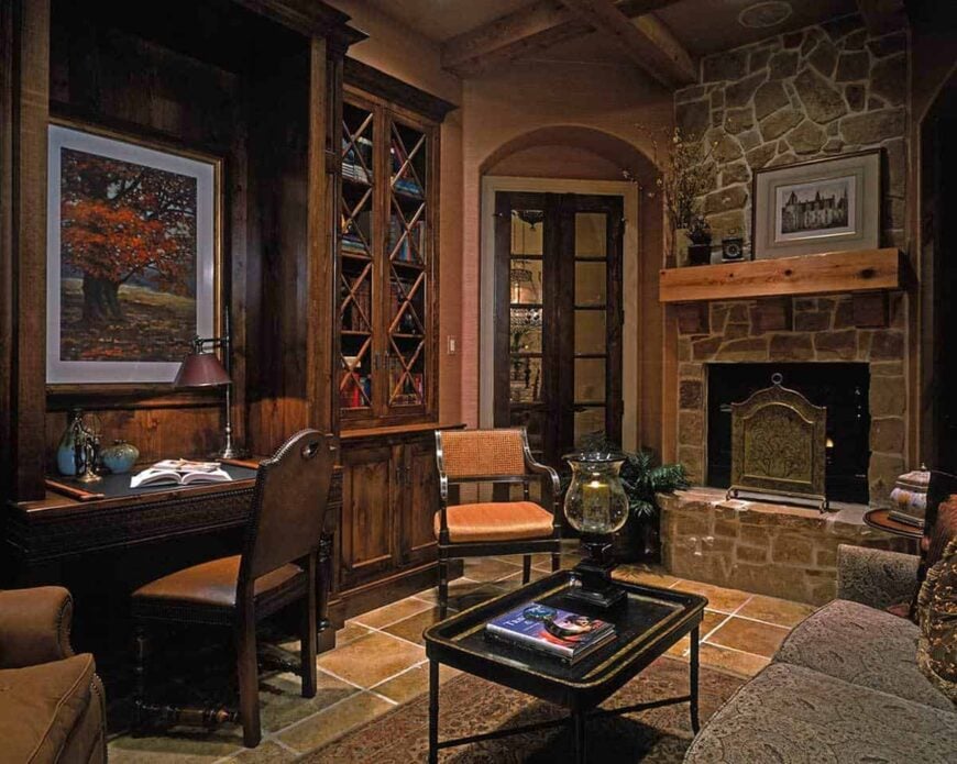 Study with a dark wood desk, a sitting area, and a stone fireplace lined with a floating shelf.