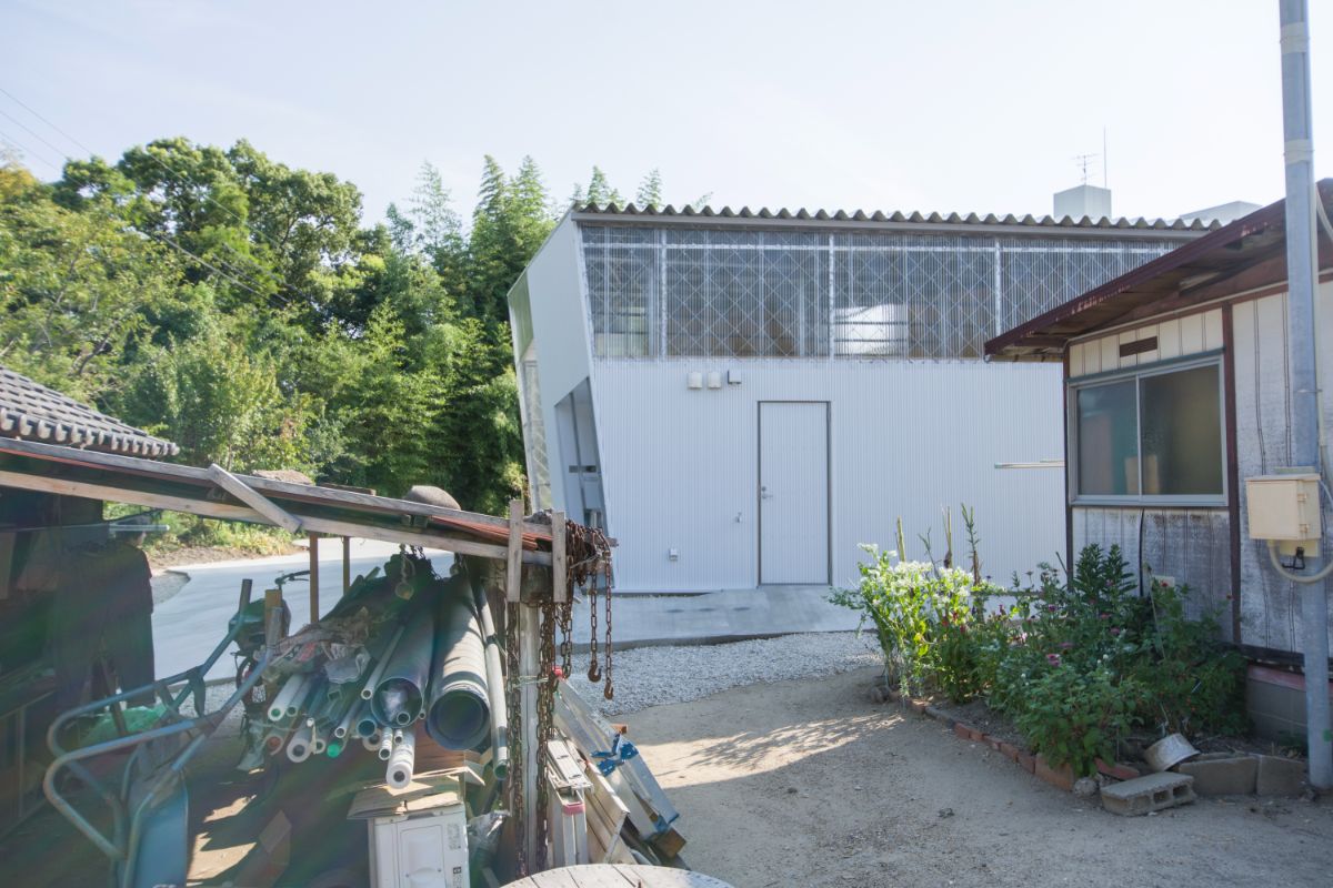 The back view of the hut-like-house with neighboring house and surrounding trees.
